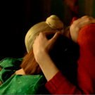 Two women, faces unseen, hold each other comfortingly. One wears green, the other red